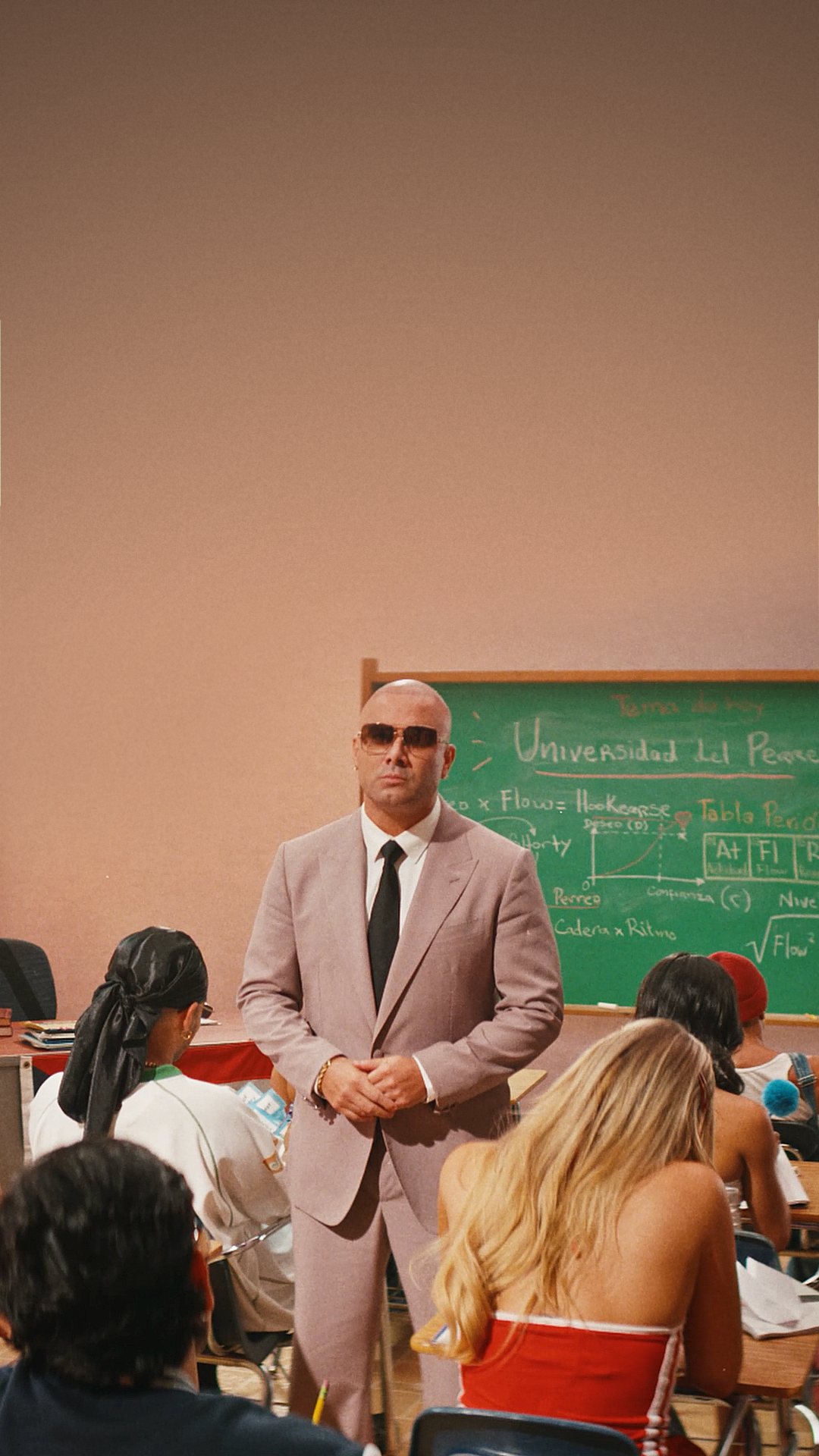 Wisin teaching in front of a chalkboard reading Universidad del Perreo