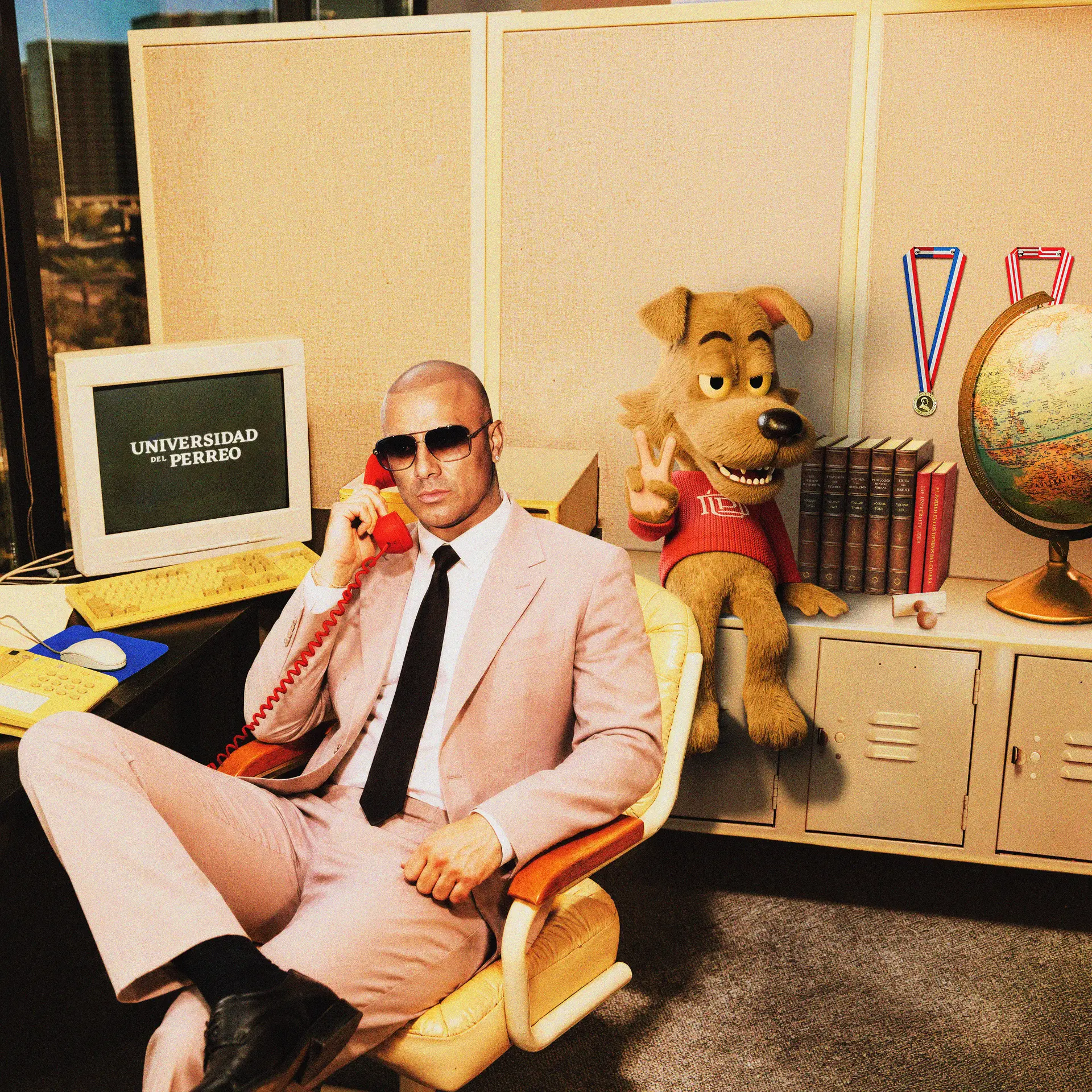 Wisin in a pink suit on the phone at the dean's desk, UDP mascot beside him